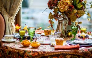 Fall tablescape with colorful gourds, fall floral arrangement, pumpkin muffins and green water and juice glasses.