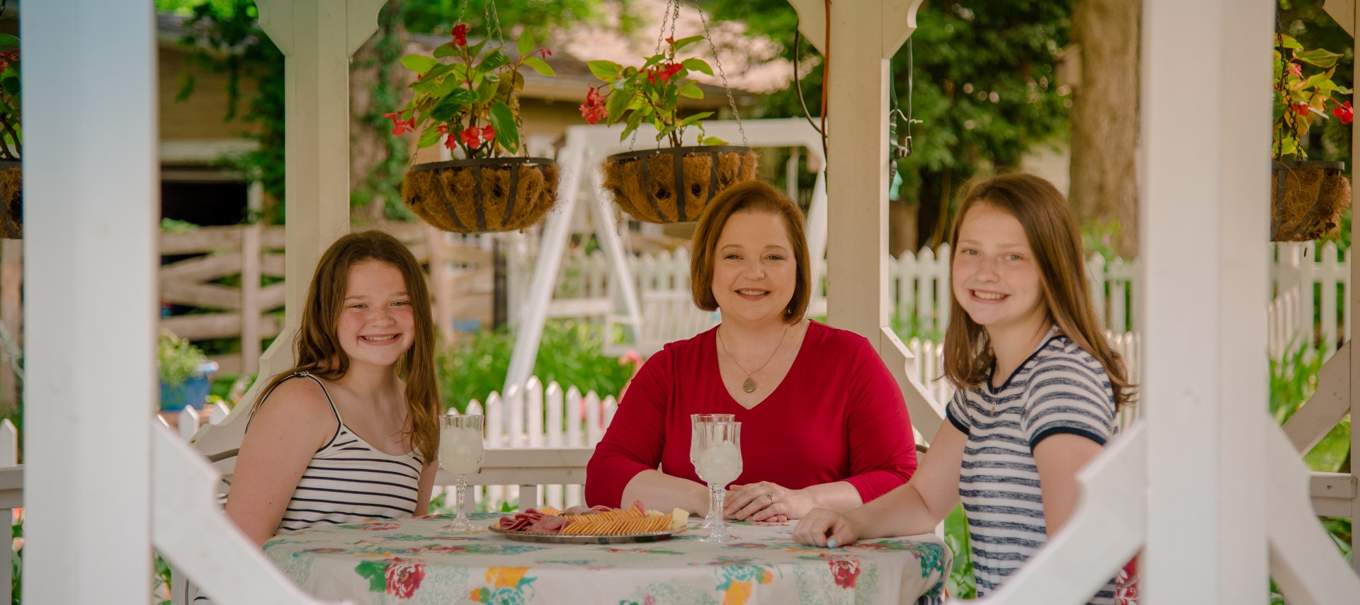 woman and two daughters sit at a table in a white gazebo