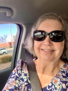 Gray haired woman wearing sunglasses riding in a car