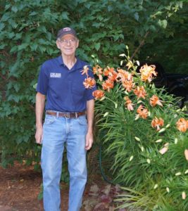 Man in blue shirt and ball cap standing next to tall lilies in bloom