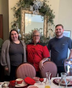 Female chef in red jacked poses with man and woman at breakfast table