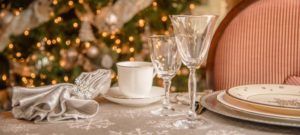 Table setting with ivory china and crystal goblens in front of a Christmas tree with white lights