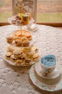 Tiered tea stand with assorted sweets and sandwiches behind a china cup and saucer.