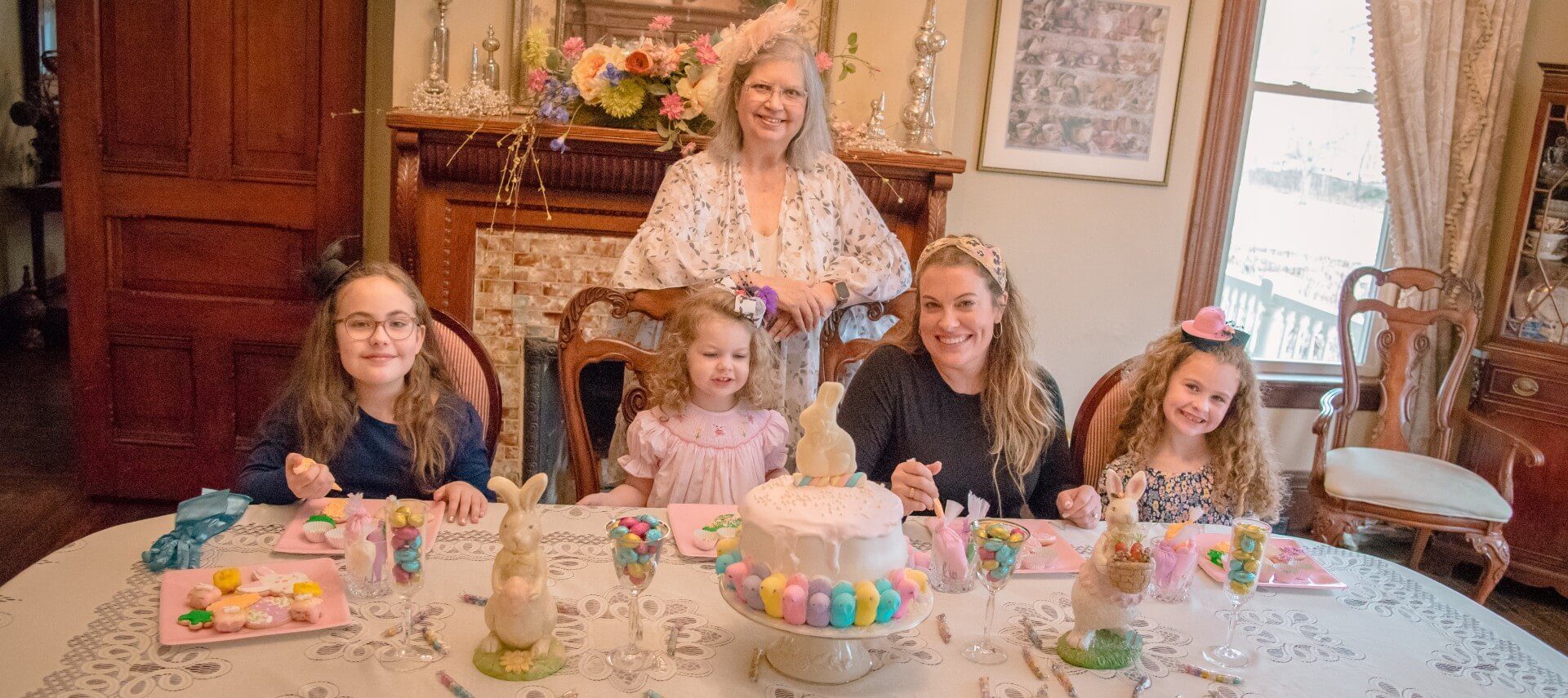 Woman poses behind a family of four female guests decorating cookies at a spring tea party