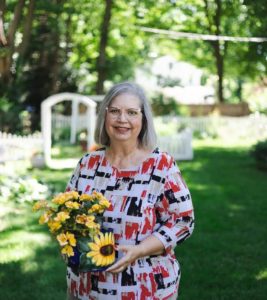 Woman with gray hair standing in the backyard holding a sunflower pot with flowers