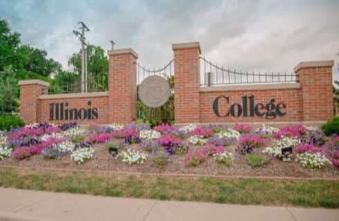 Large red brick sign for Illinois College surrounded by purple, pink, and white flowers