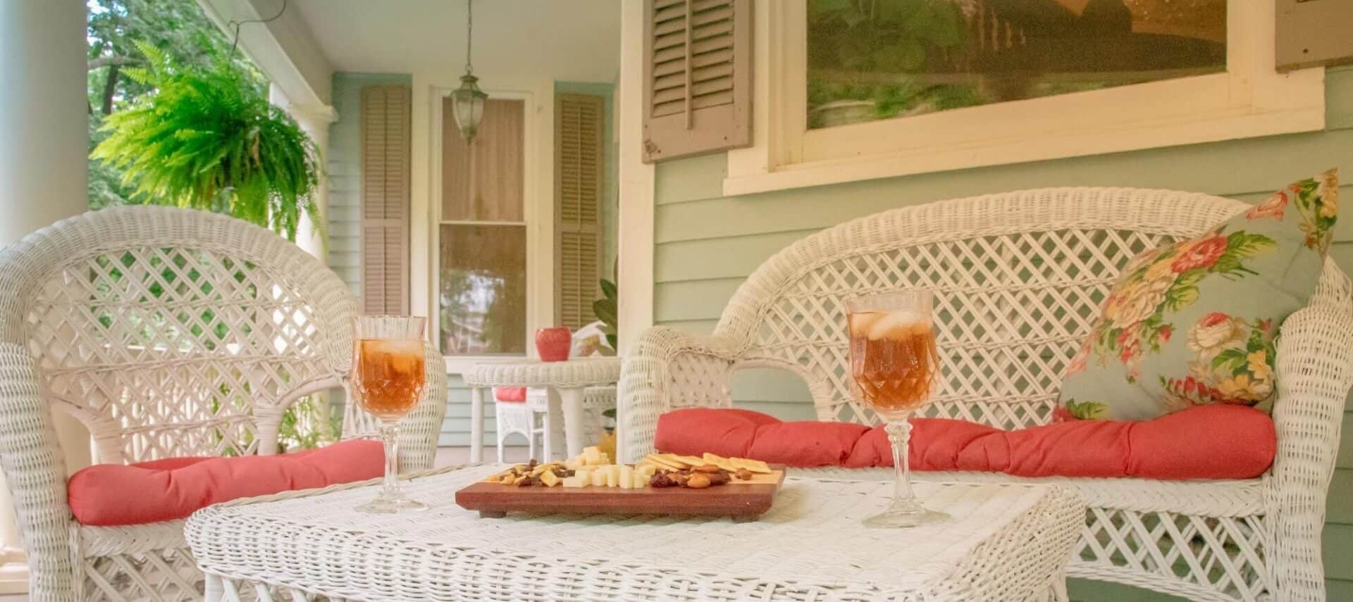 close up of meat and cheese board and iced tea on a white wicker table surrounded by wicker chairs