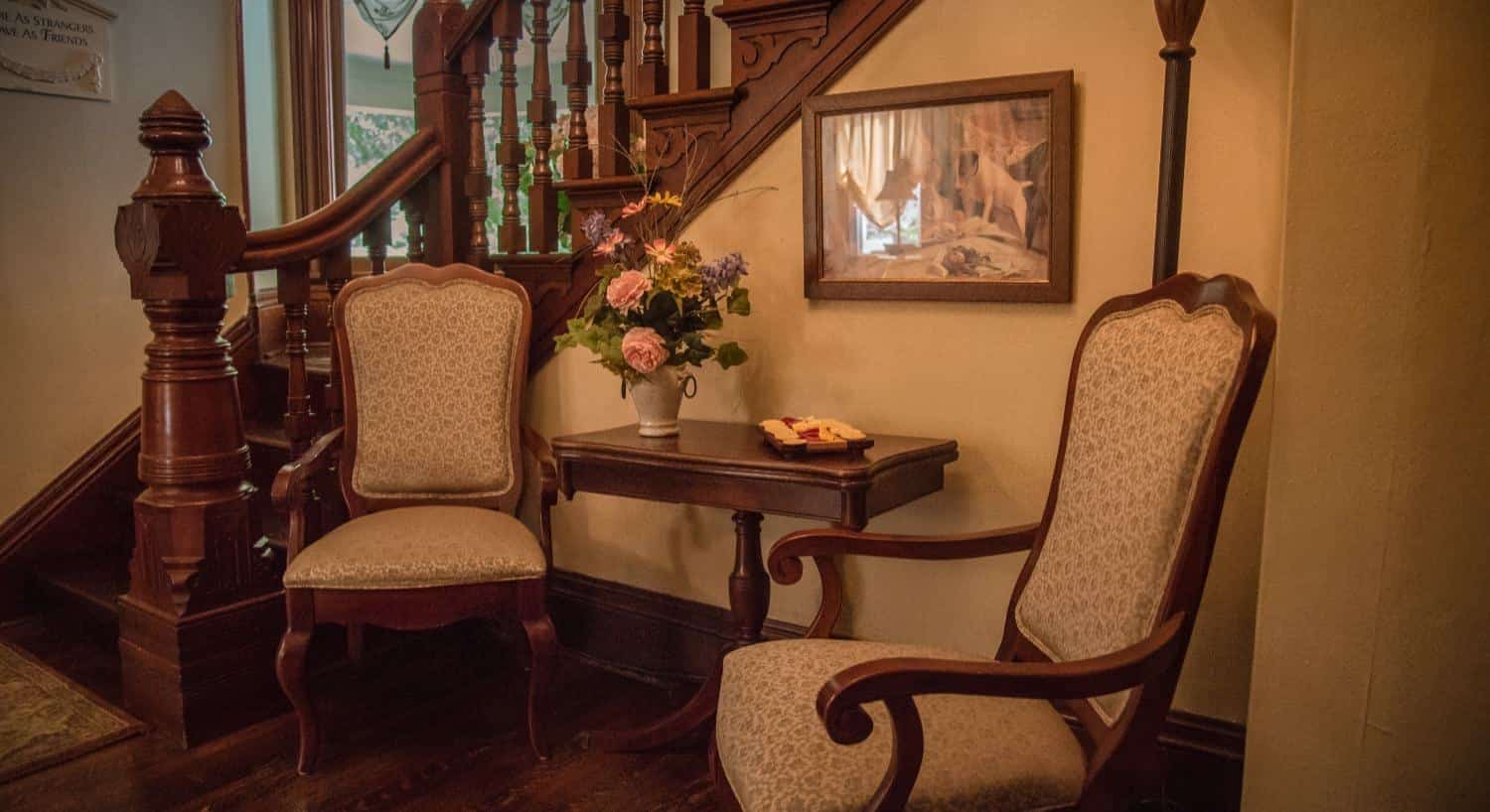 Two Victorian wooden chairs with upholstered backs and bottoms sitting next to wooden staircase