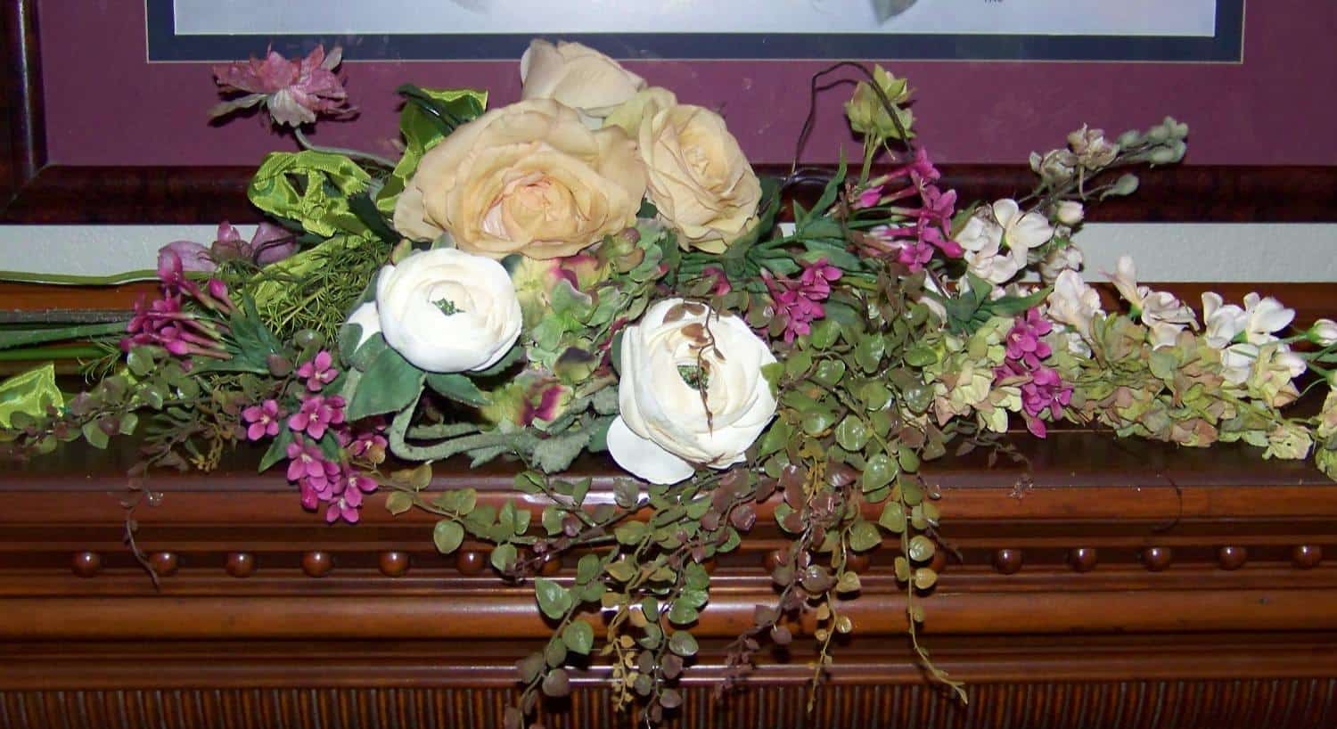 Close up view of white and cream roses, pink and purple flowers, and greenery on top of wooden mantel
