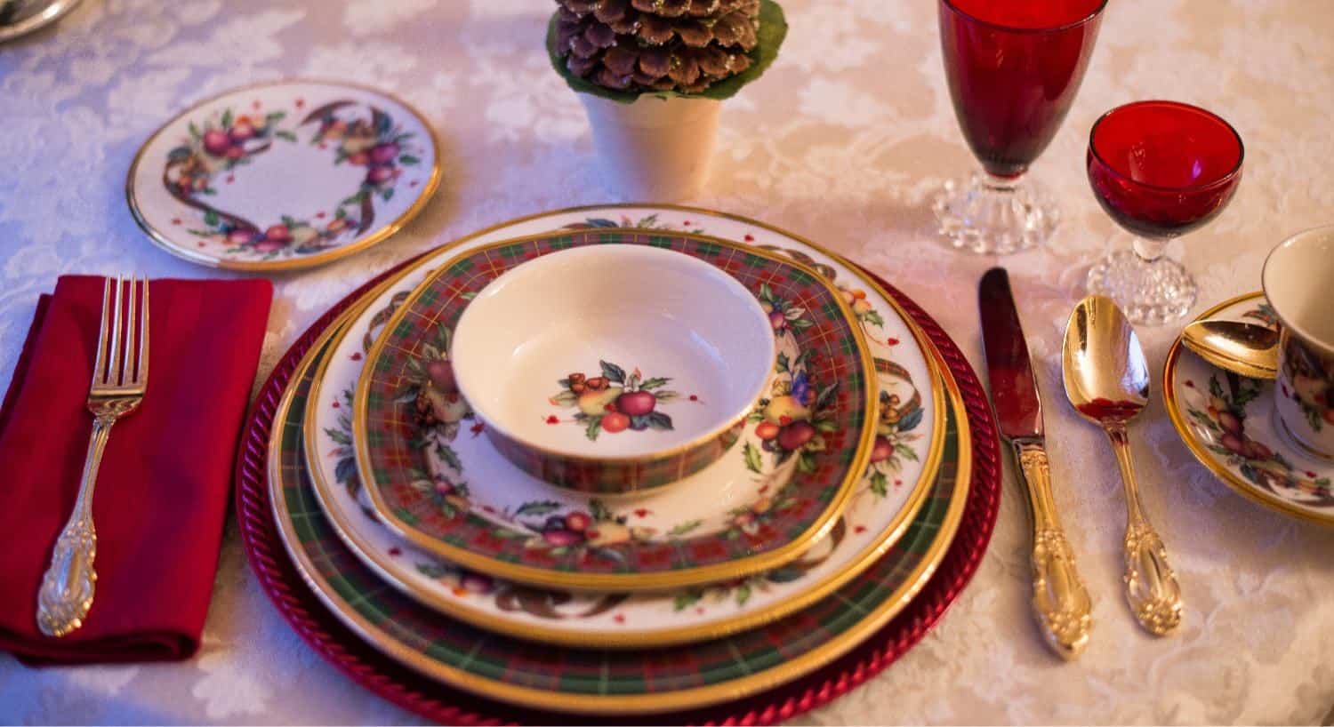 Plaid and fruit decorated fine china place setting with gold plated silverware, red napkin, and red glasses