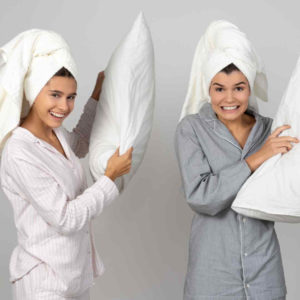 two women wearing towels on their heads having a pillow fight