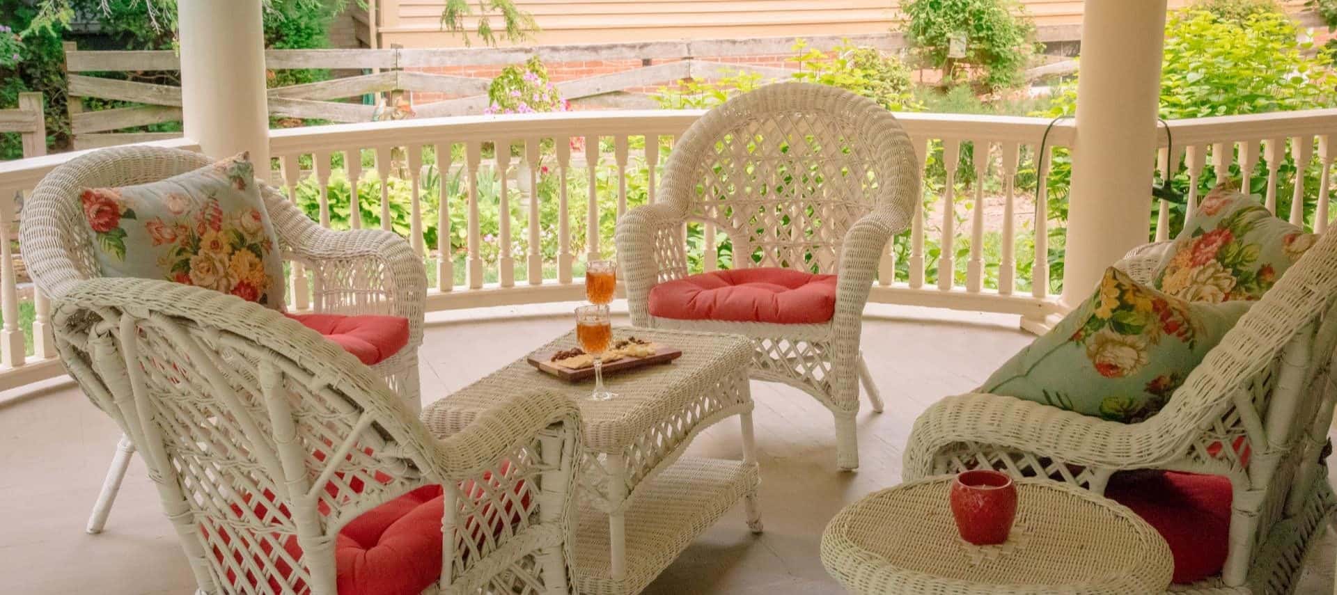 White wicker patio furniture with coral and floral cushions and pillows on front porch