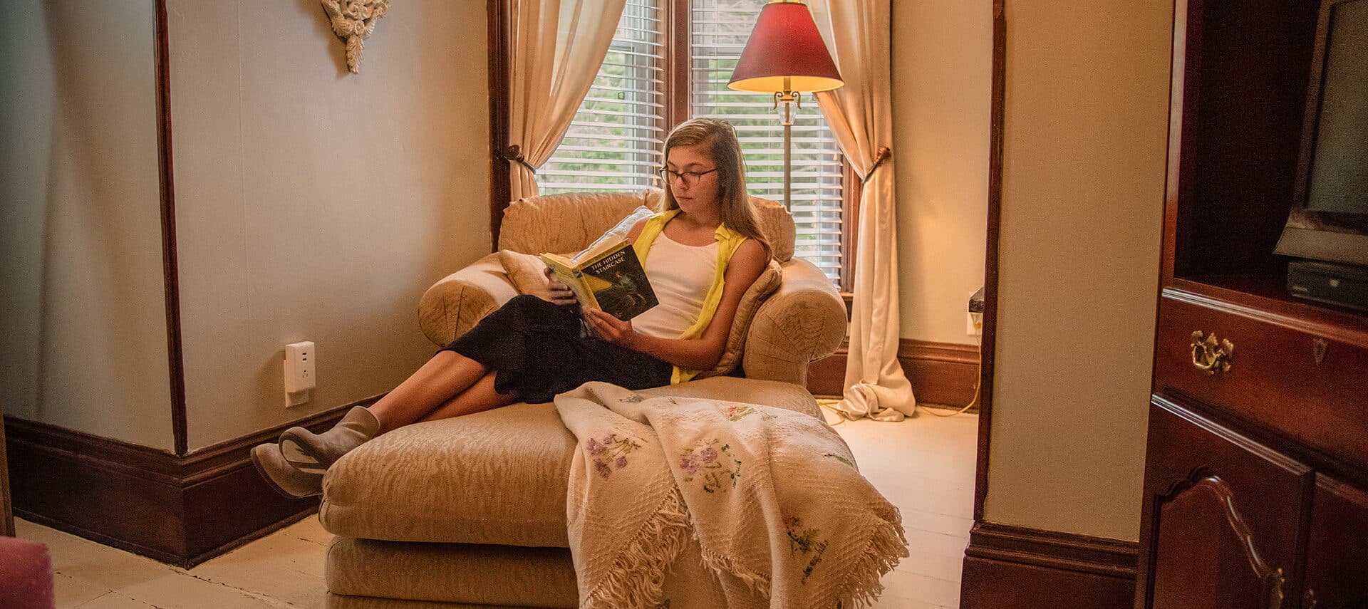 young lady reading a book while sitting on a chaise