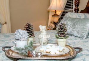 Snowflake cookie tray with snowman and pinecones on bed with blue cover and pillows