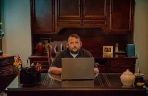 Man sitting at wooden desk behind a laptop