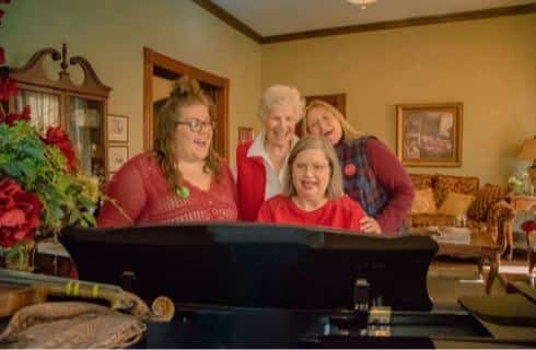 Four ladies smiling and singing songs around a piano