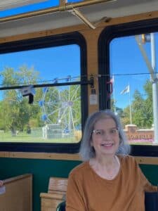 Gwenn inside a trolley, with a background of the Jacksonville Ferris Wheel and accompanying sign