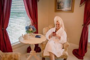 woman in fluffy white robe with white towel on her head sitting in a side chair with a mug of coffee